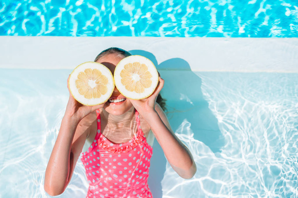 Menina cobrindo os olhos com metades de limão perto de olhos na piscina de fundo - Foto, Imagem