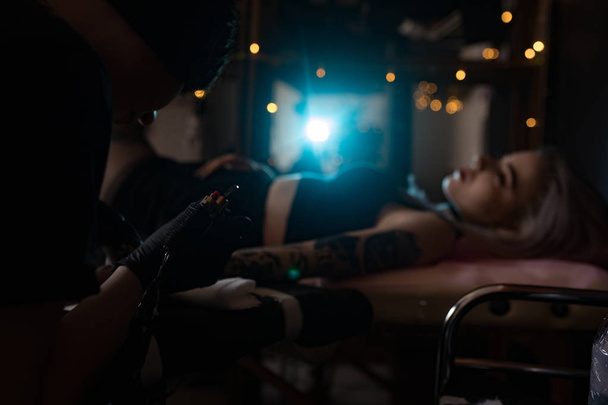 Tattoo artist creates a tattoo on a girl's arm in tattoo parlour - Photo, image