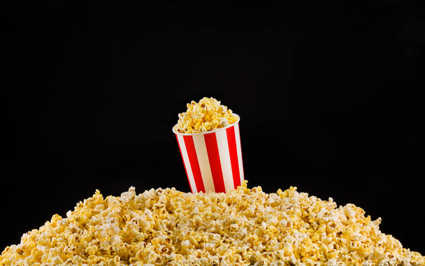 Paper striped bucket installed on scattered popcorn isolated on black background - 写真・画像