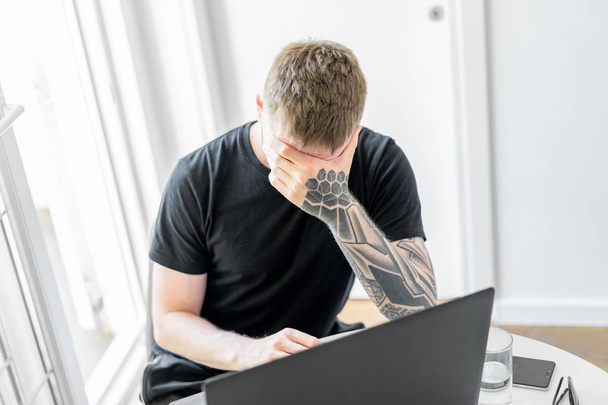 Handsome pensive man working on laptop in modern bright apartments. - Фото, изображение