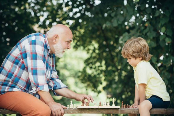 Little boy playing chess with his Grandfather. Chess piece. Senior man thinking about his next move in a game of chess. Grandfather playing chess with his grandson. - Фото, зображення