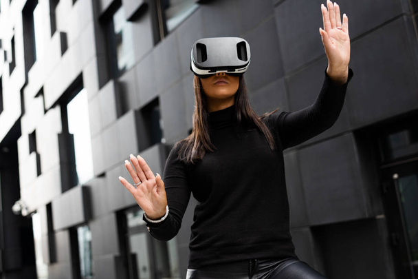 Kobieta za pomocą wirtualnej rzeczywistości okulary i noszenie czarny w futurystycznym mieście - Zdjęcie, obraz