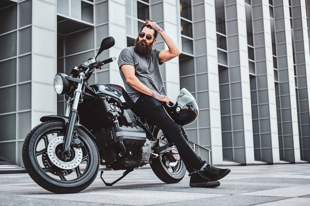 Портрет бородатого байкера, отдыхающего со своим мотоциклом
 - Фото, изображение