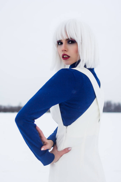 Tyttö valkoisessa peruukissa talvella pellolla sinisessä poolopaidassa
 - Valokuva, kuva