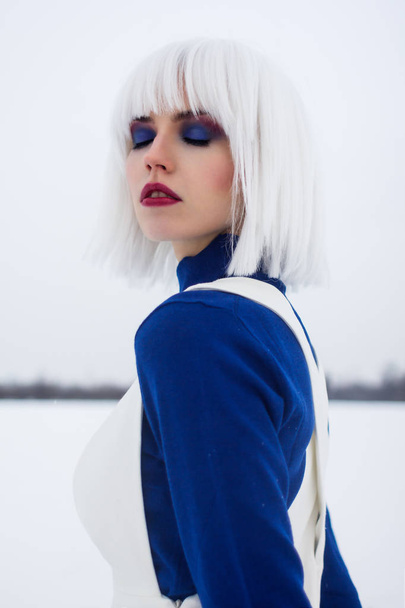 chica en una peluca blanca en invierno en un campo en un cuello alto azul
 - Foto, Imagen