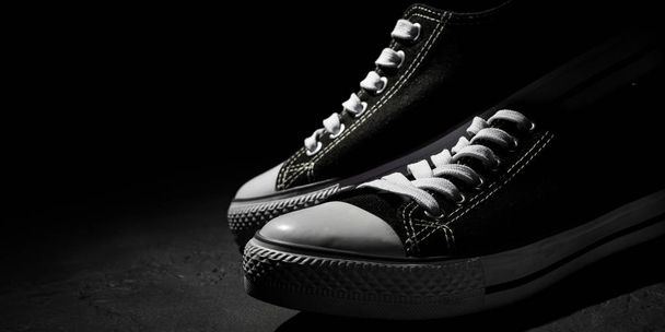 Pair of new black sneakers on dark black background with copy space. - Фото, изображение