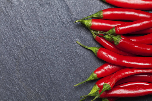 Rode verse chili pepers op een donkere leisteen achtergrond - Foto, afbeelding