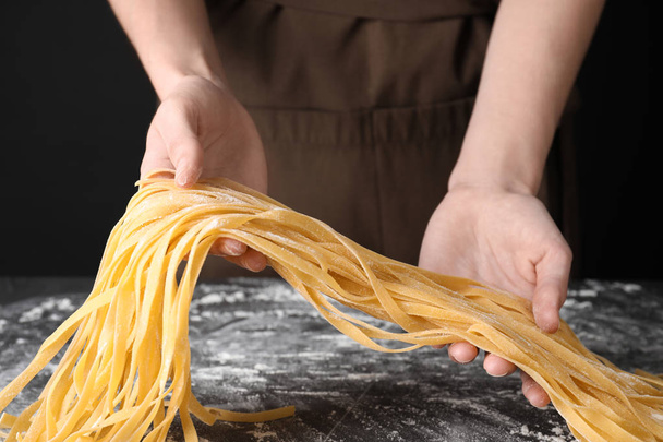Woman holding raw egg noodles over grey table, closeup - Foto, afbeelding