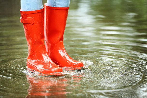 Woman with red rubber boots in puddle, closeup. Rainy weather - Zdjęcie, obraz