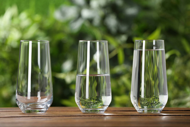 Empty, half and full glasses of water on wooden table against blurred background - Foto, Bild