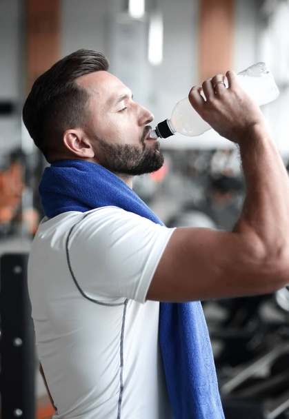 Young adult man drinking bottle of water on trreadmill in gym. - Фото, изображение