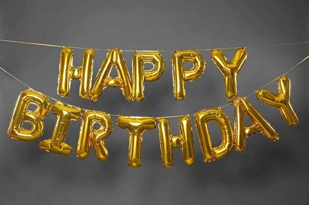 Phrase HAPPY BIRTHDAY made of golden balloon letters on grey background - Foto, immagini