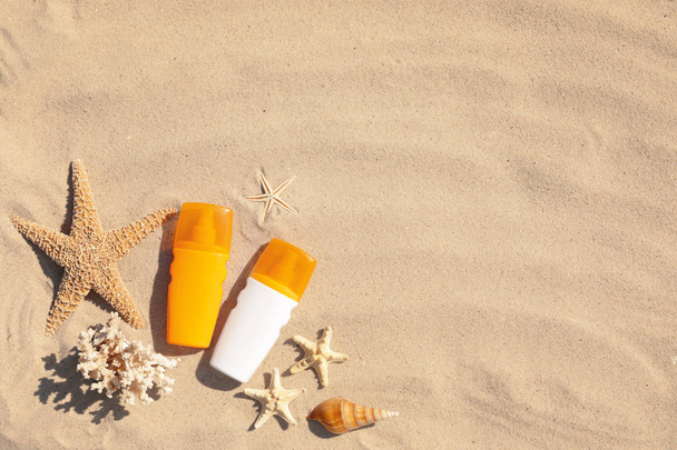 Flat lay composition with bottles of sunblock on sandy beach. Space for text - Фото, изображение