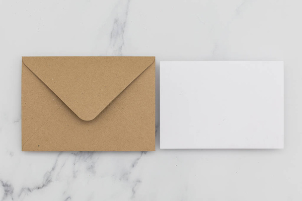 Blank white card with kraft brown paper envelope on marble backg - Fotoğraf, Görsel