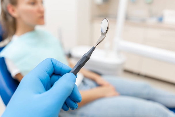 Close-up hand of dentist in the glove holds tool probe and mirror. The patient in the dental chair at the background. Dental work in clinic. Office where dentist conducts inspection and concludes. - Foto, Imagem