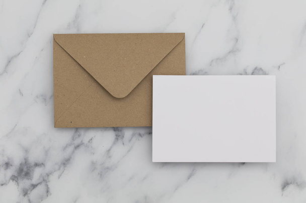 Blank white card with kraft brown paper envelope on marble backg - Fotó, kép