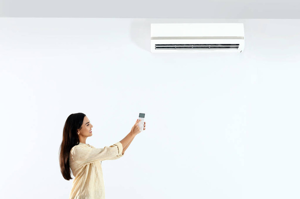 Young woman turning on air conditioner against white background - Photo, Image