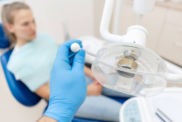 Close-up hand of dentist in the glove adjusts the lamp. The patient in blue chair at the background. Office where dentist conducts inspection and concludes. - 写真・画像