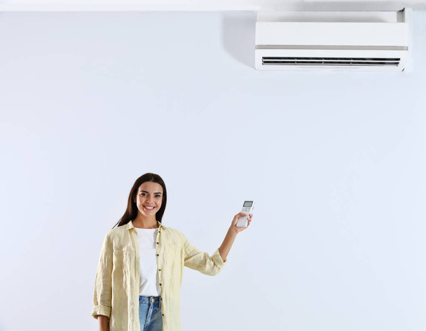 Young woman turning on air conditioner against white background - Foto, Bild