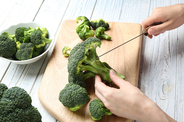 Woman cutting fresh green broccoli with knife on white wooden table, closeup view - Foto, Imagem
