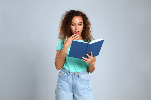 Beautiful African-American young woman reading book on light background - Φωτογραφία, εικόνα