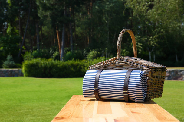 Picnic basket with blanket on wooden table in green park - 写真・画像