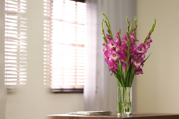 Vase with beautiful pink gladiolus flowers on wooden table in room, space for text - Foto, Imagem