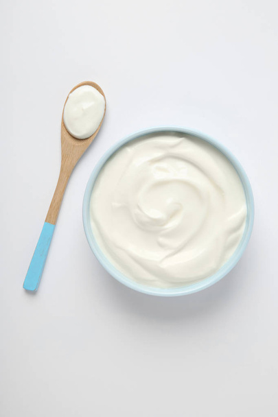 Bowl of sour cream and wooden spoon on white background, top view - Φωτογραφία, εικόνα