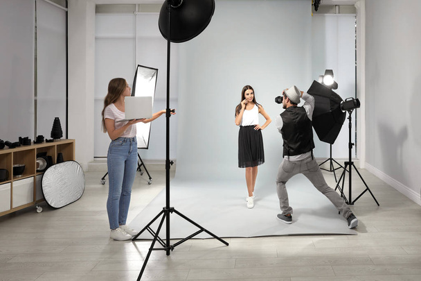 Professional photographer with assistant taking picture of young woman in modern studio - 写真・画像