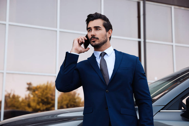 Attractive young man talking on phone near luxury car outdoors - Φωτογραφία, εικόνα