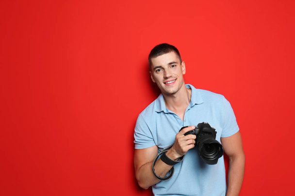Young photographer with professional camera on red background. Space for text - Foto, afbeelding