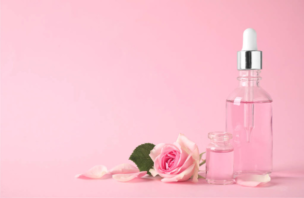 Bottles of essential oil and rose on pink background. Space for text - 写真・画像