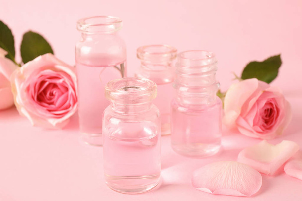 Bottles of essential oil and roses on pink background - Foto, Imagen