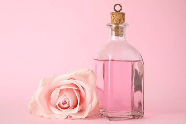 Bottle of essential oil and rose on pink background - Foto, imagen