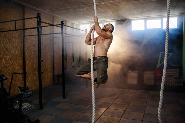 Strong young crossfitter climbing on the rope during training. - Foto, immagini