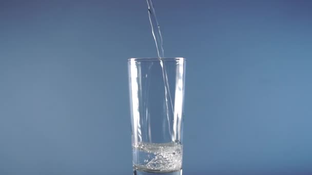 Tiszta víz Önt egy pohár serleget a tetejről egy kék gyönyörű háttér - Felvétel, videó