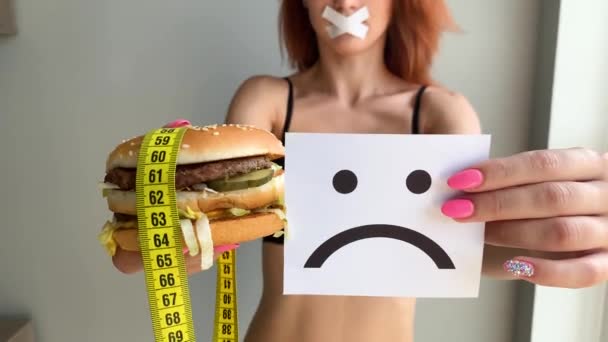 Diety. Portret kobiety chce jeść Burger, ale klejone usta, pojęcie diety, niezdrowej żywności, woli w żywieniu - Materiał filmowy, wideo