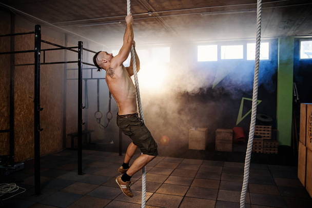 Strong young crossfitter climbing on the rope during training. - Foto, imagen