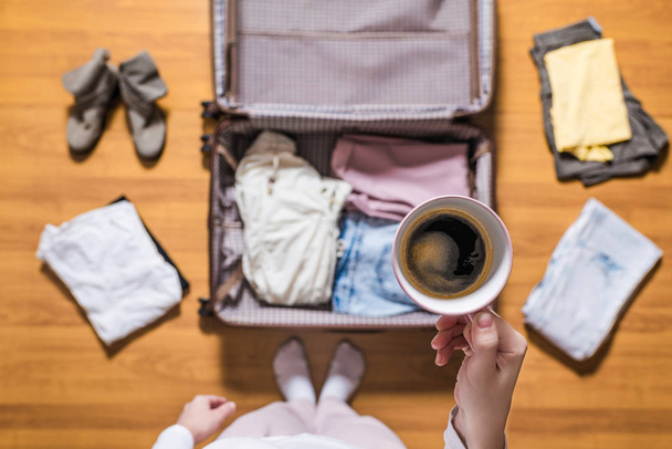 Top view of woman hands packing a luggage for a new journey and drinking coffee from the pink cup .  - Fotó, kép