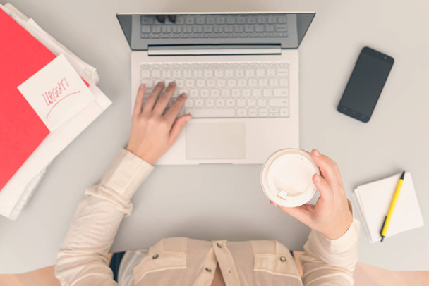 Business woman drinks coffee from paper cups while working on the laptop in an office. Top view - Фото, зображення
