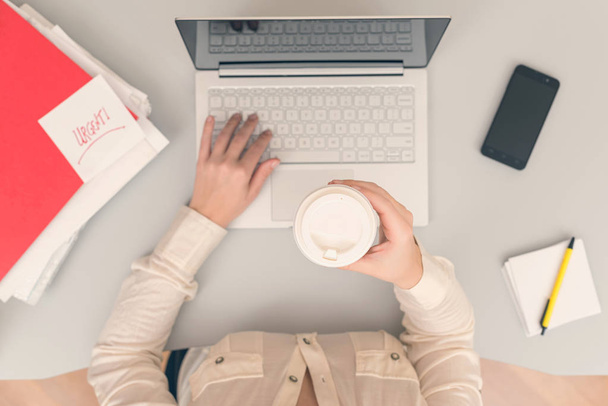 Business woman drinks coffee from paper cups while working on the laptop in an office. Top view - Photo, image