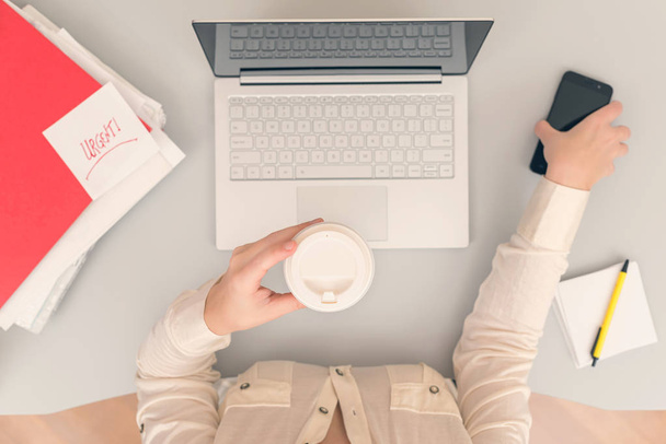 Geschäftsfrau trinkt Kaffee aus Pappbechern, während sie in einem Büro am Laptop arbeitet. Ansicht von oben - Foto, Bild