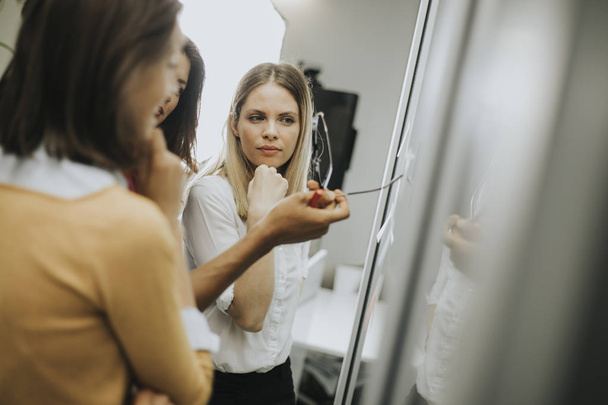 Группа молодых деловых женщин обсуждают перед стеклянной стеной, используя посты и наклейки в офисе стартапа
 - Фото, изображение