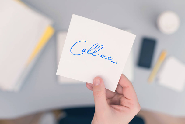 Woman clerk in the office holding paper sticker with the word call me. concept  - Photo, Image