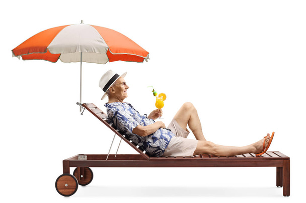 Senior Mann entspannt sich auf einem Strandbett unter einem Sonnenschirm mit einem Cocktai - Foto, Bild