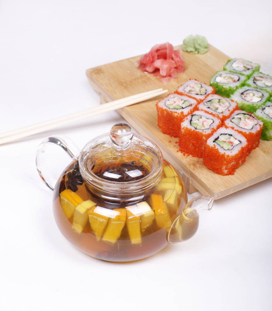 tetera de vidrio con té de frutas y juego de rollos japoneses en placa de madera
  - Foto, Imagen