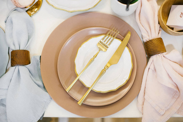 Set of beige and white ceramic plates with gold cutlery and linen napkins on festive wedding table.  - Fotoğraf, Görsel