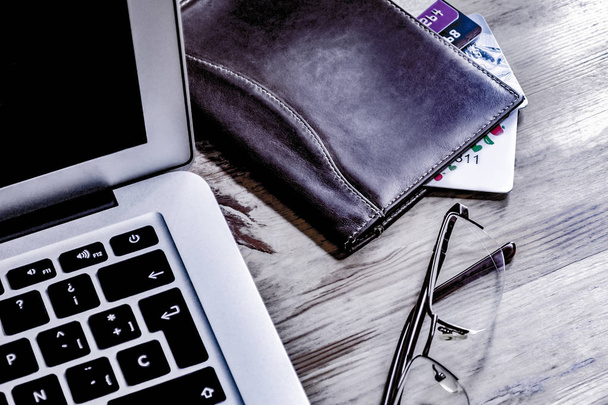 Очки, ноутбук, кредитные карты в кожаном бумажнике на деревянном столе
 - Фото, изображение