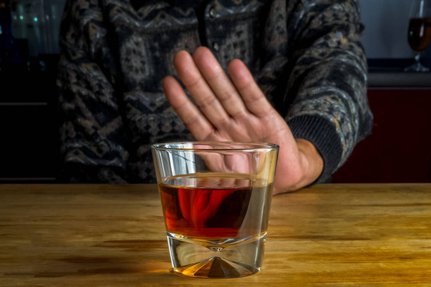 Мужская рука отвергает стекло с алкогольным напитком на размытом пакете
 - Фото, изображение