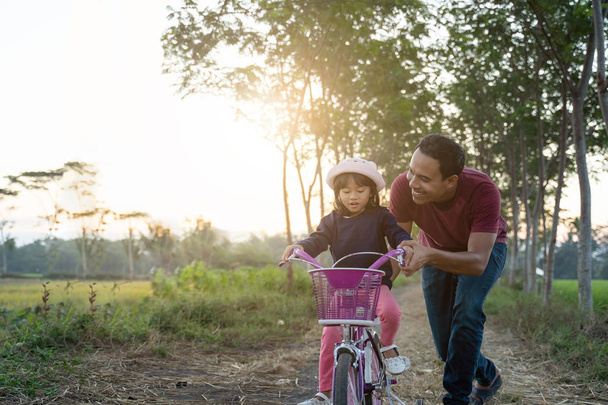 asian dad help her kid to ride bicycle outdoor - Fotoğraf, Görsel